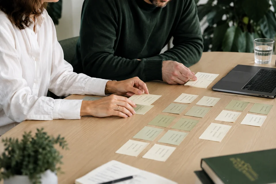 Strategists organizing research cards into groups beside a laptop