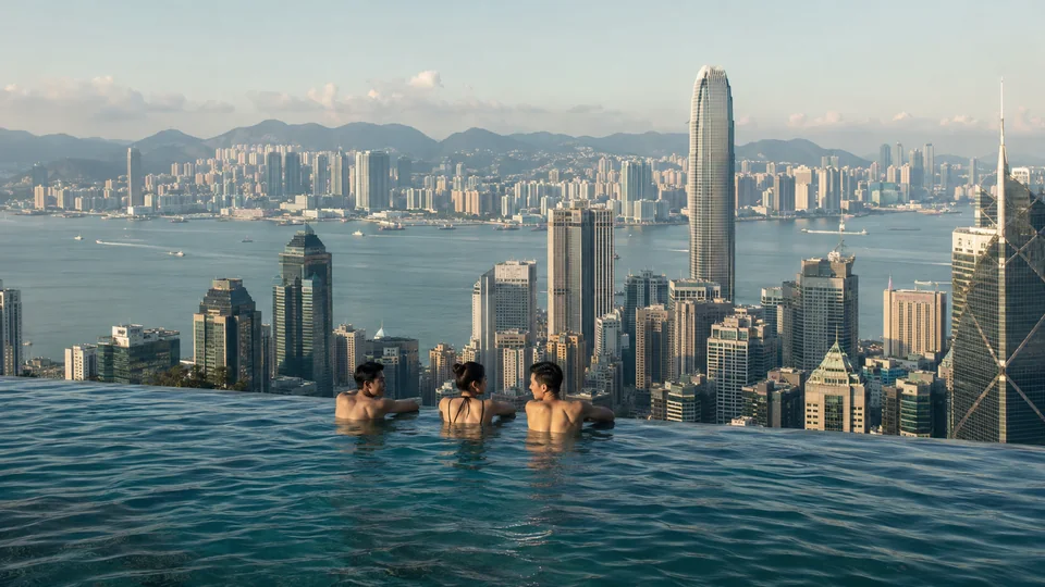 People at a high-rise infinity pool overlooking Victoria Harbour and Hong Kong’s financial skyline